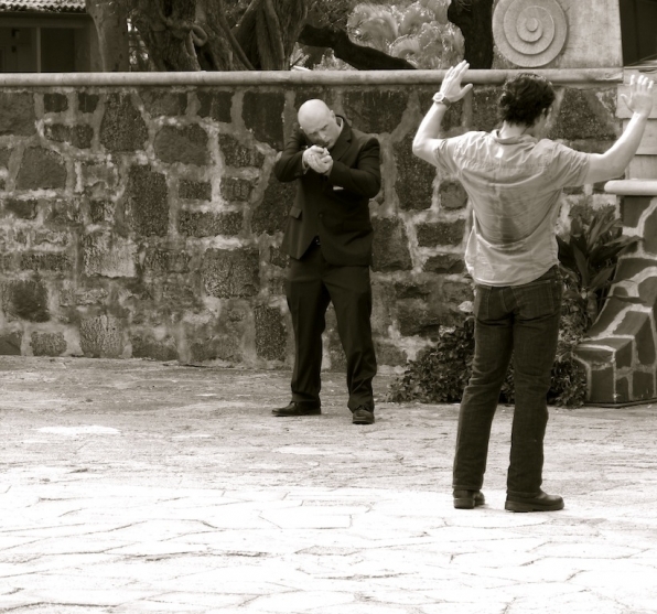 Un homme pointe son arme sur Chin (Daniel Dae Kim) qui lève les mains en l'air.