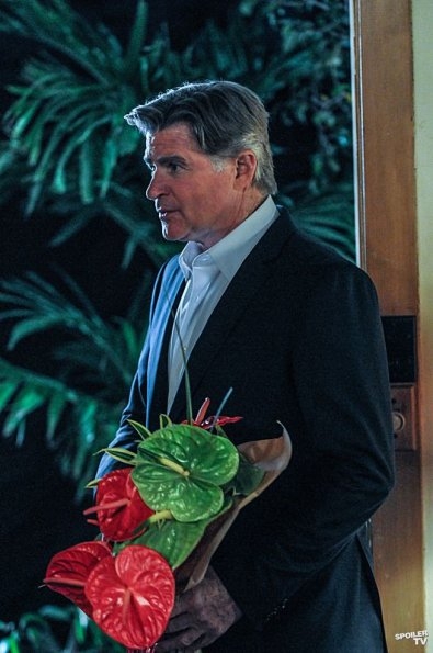 Mick Logan (Treat Williams) est vêtu d'un costard noir et tient dans ses mains un bouquet de fleurs.