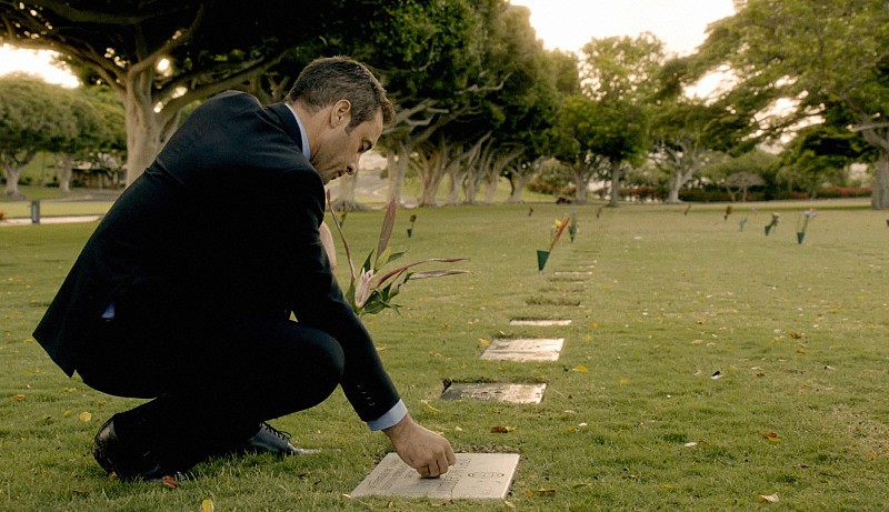 Steve (Alex O'Loughlin) dépose quelque chose sur la pierre tombale de son père.
