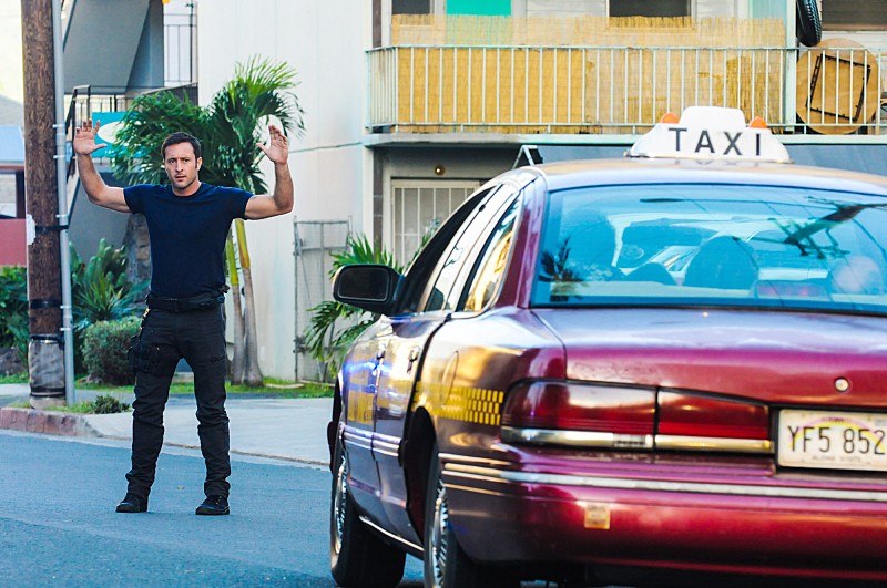 Steve (Alex O'Loughlin) met les mains en l'air alors qu'il est face à un taxi.