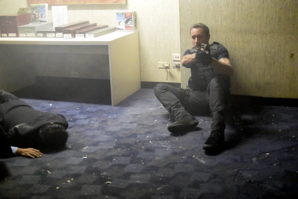 Steve McGarrett (Alex O'Loughlin) dégaine son arme après l'explosion alors qu'il est assis sur le sol.