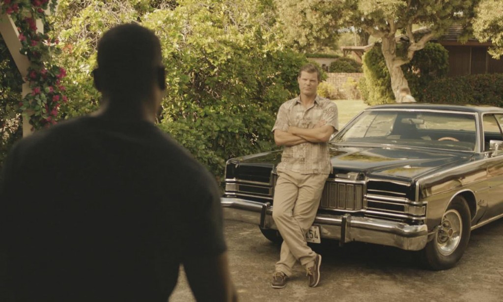 John McGarrett se tient debout contre sa voiture (Mercury Marquis) avec les bras croisés. Un autre homme vient à sa rencontre...