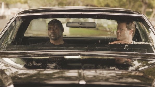 Quelques années plus tôt, John McGarrett (Ryan Bittle) discute avec Leroy Davis (Thomas Q. Jones) dans une voiture.
