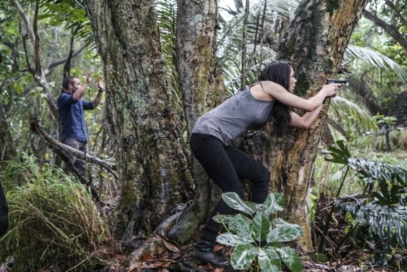 Alors que Steve (Alex O'Loughlin) lève les mains en l'air, Catherine (Michelle Borth) qui est cachée derrière un arbre va essayer de l'aider...