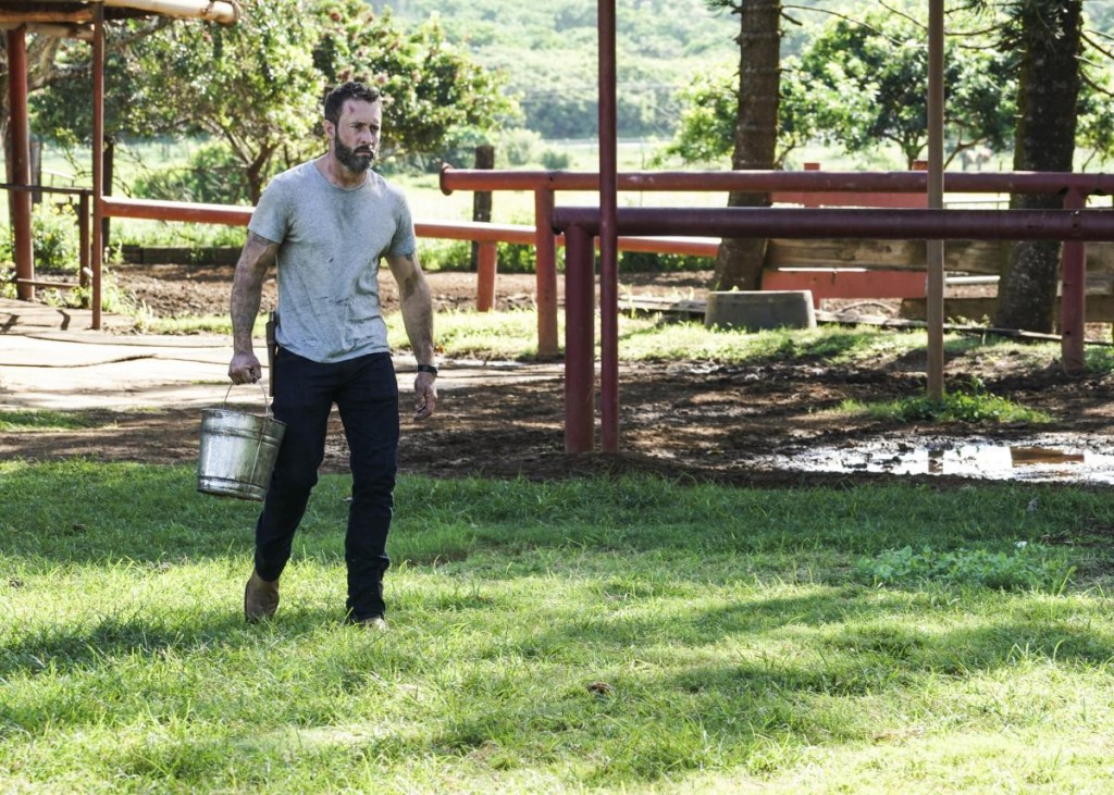 Steve (Alex O'Loughlin) marche avec un seau d'eau à la main.