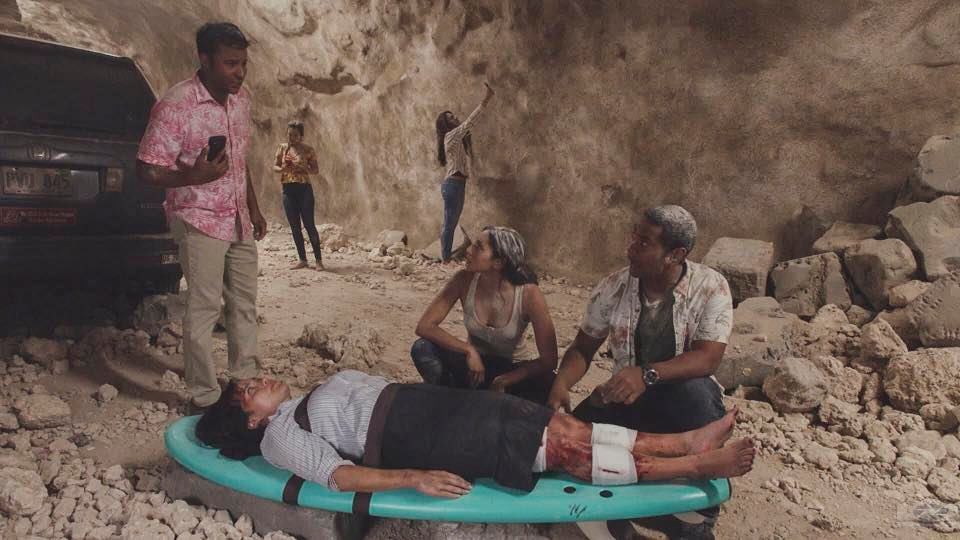 Tani (Meaghan Rath) et Junior (Beulah Koale) sont auprès d'une femme blessée et discutent avec un homme ayant une chemise hawaiienne.