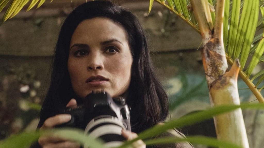 Quinn (Katrina Law) tient un appareil photo entre ses mains.