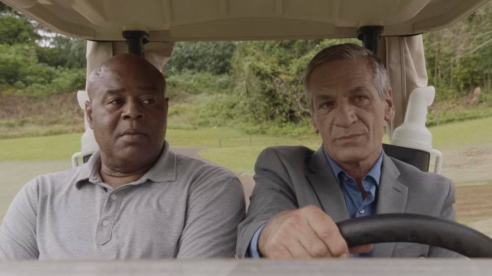 Grover (Chi McBride) est assis dans une voiturette de golf en compagnie d'un homme en costard.