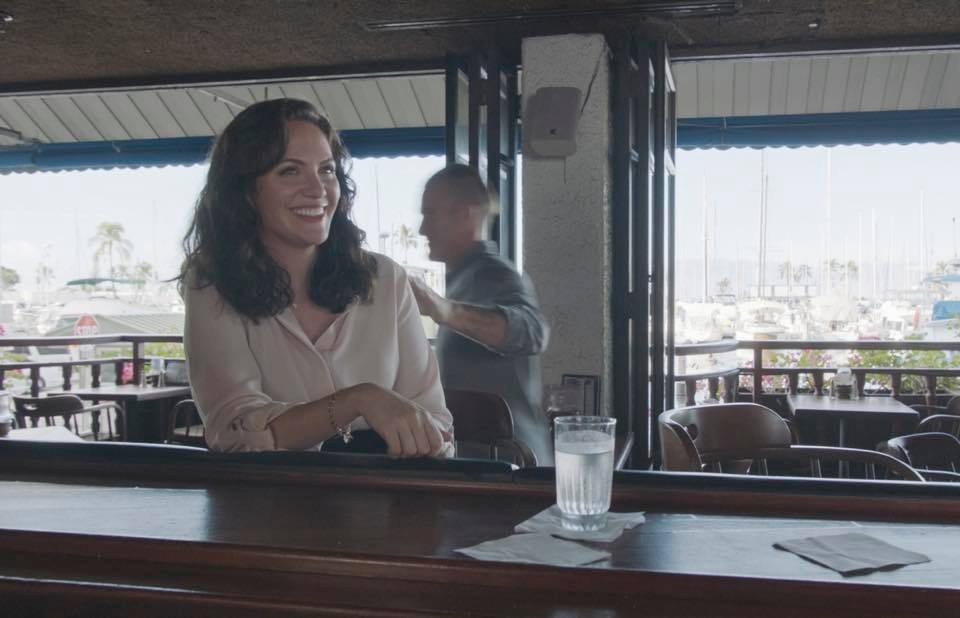 Alors que Danny (Scott Caan) s'éloigne pour prendre un appel, Joanna (Kate Siegel) reste au bar, souriante.